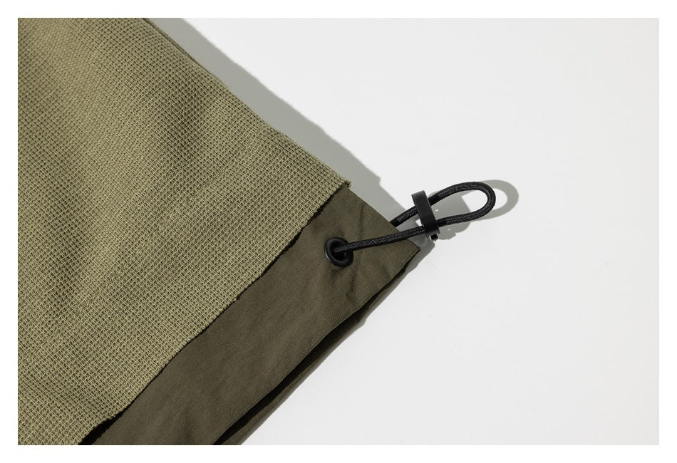 Close-up of an olive-green shirt hem with a black adjustable drawcord and cord lock.