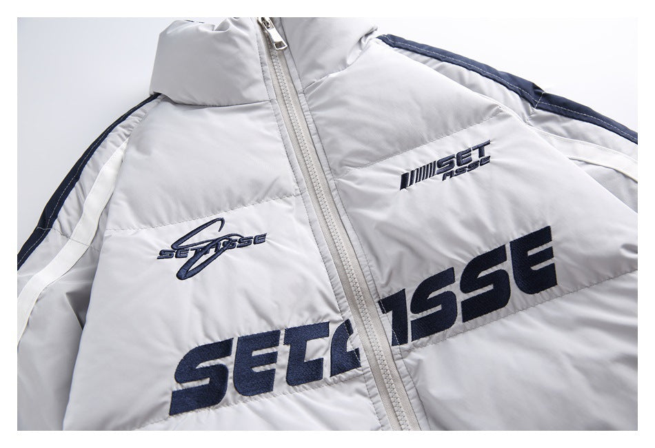 Close-up of the light gray jacket’s front zipper and navy embroidered chest graphics, with white and navy sleeve stripes.