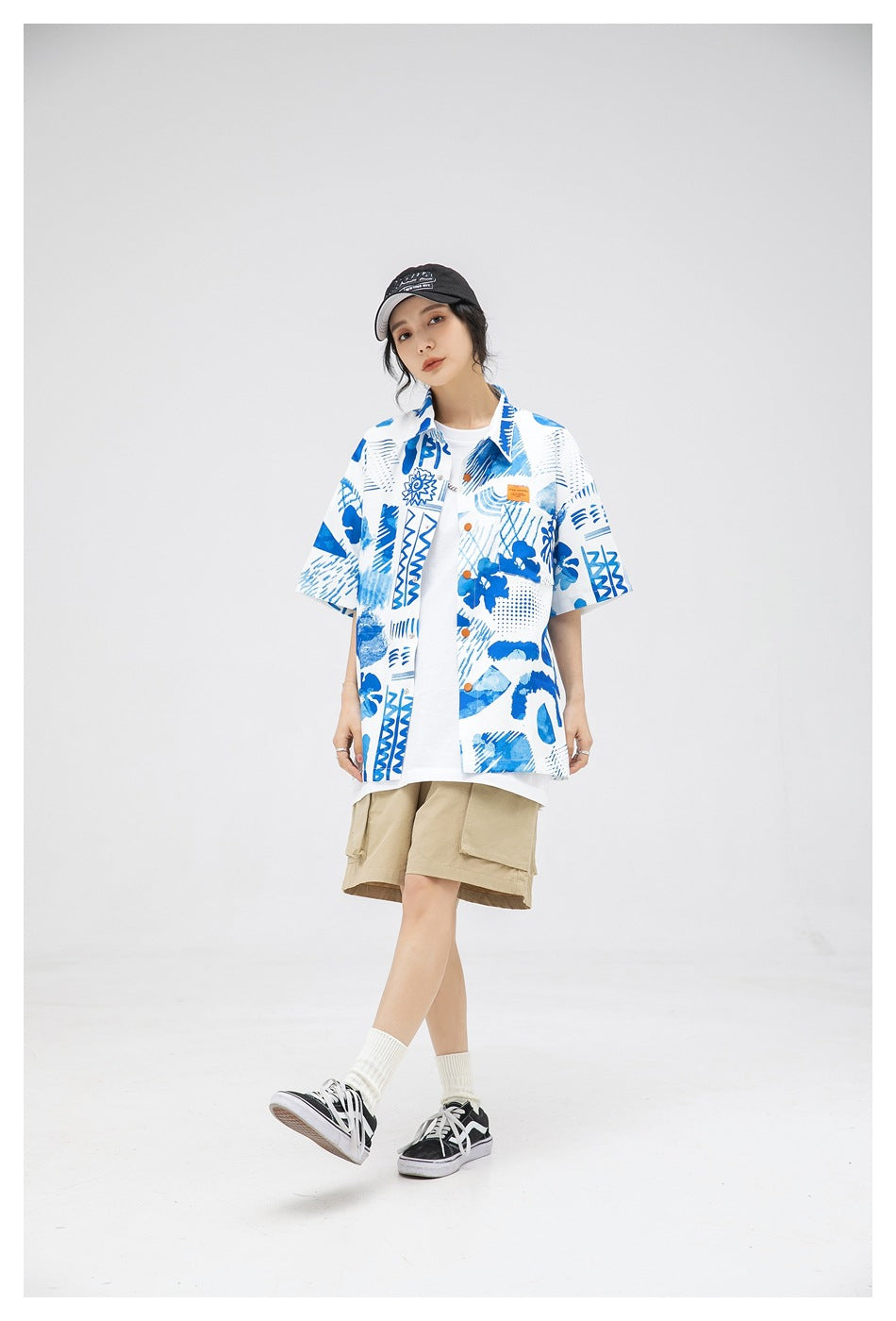 Model wearing a blue-and-white abstract print short-sleeve shirt over a white tee with beige shorts.