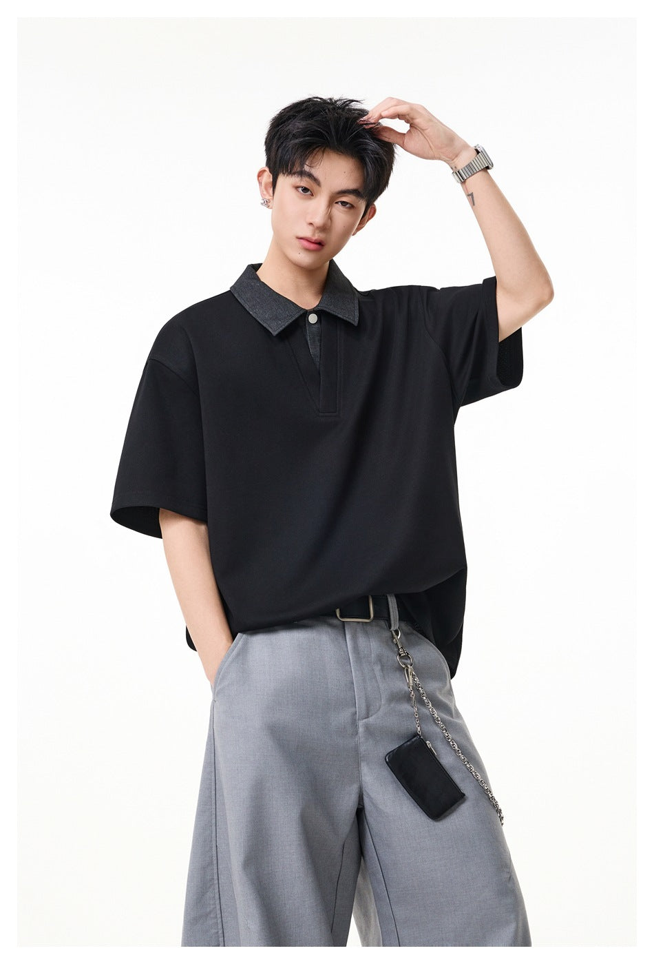 Model with hand raised wearing black short-sleeve polo top with gray collar and gray trousers