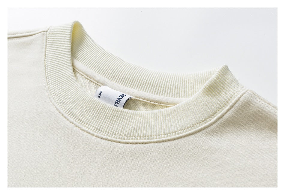 Close-up of a cream sweatshirt’s ribbed crew neckline and inner neck label.