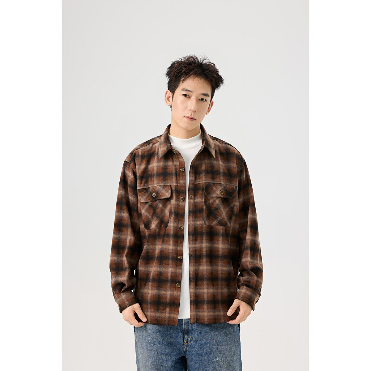 Closer front view of a model wearing a brown plaid button-up overshirt with two flap chest pockets over a white top.