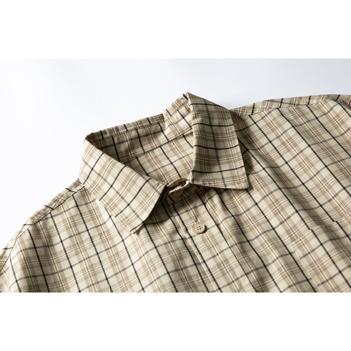 Close-up of a beige plaid short-sleeve shirt showing its pointed collar, button placket, and chest pocket edge.