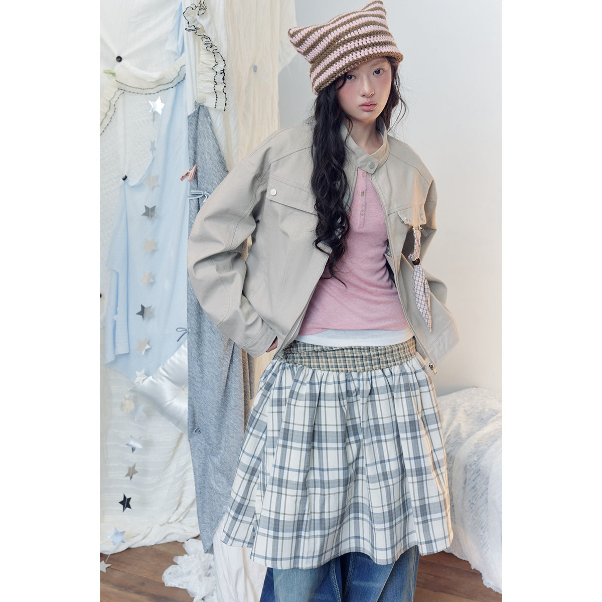 Closer view of a model in a light gray jacket with a plaid bow detail and a gray-and-cream plaid skirt.