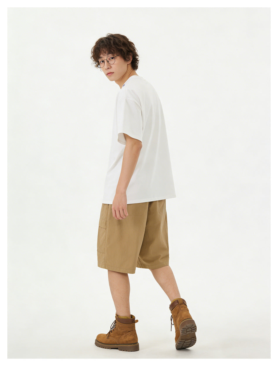 Model in a white T-shirt and tan cargo shorts, turned to show the shirt's side and back with brown boots.