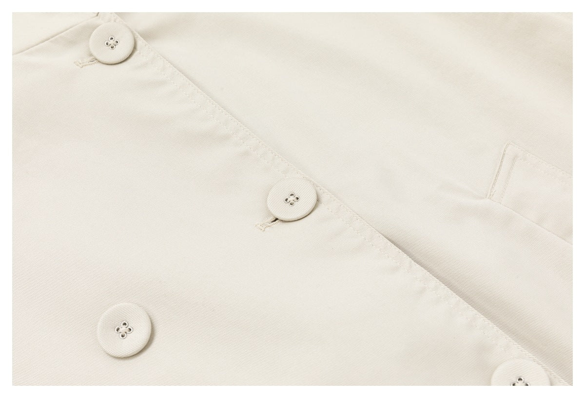 Close-up of the light beige coat front with matching buttons and the edge of a pocket.