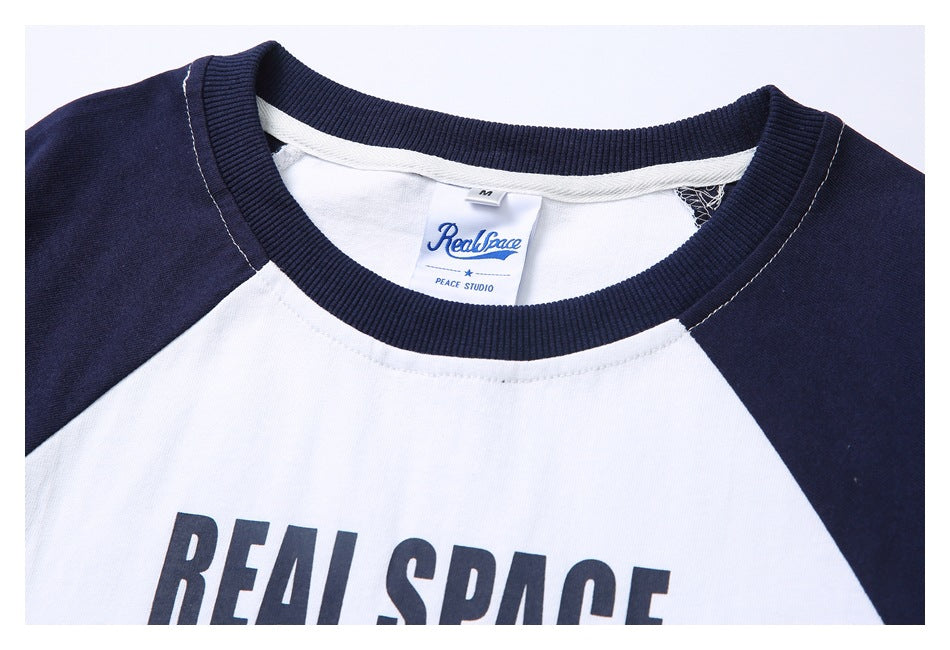 Close-up of the navy ribbed neckline, RealSpace label, and upper chest graphic on a white-and-navy raglan T-shirt.