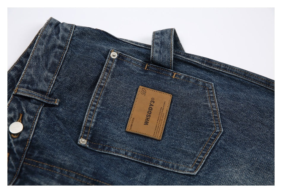 Close view of the back of dark blue jeans, showing a rear pocket, belt loops and a tan leather label.