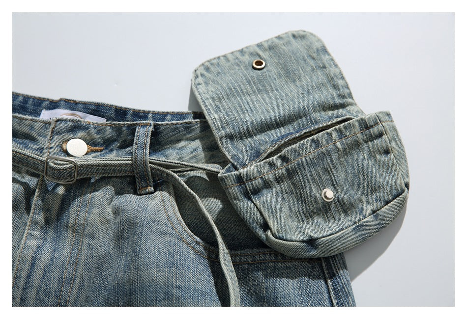 Close-up of the jeans' waist with a buckle strap and a folded denim flap pocket secured by metal hardware.