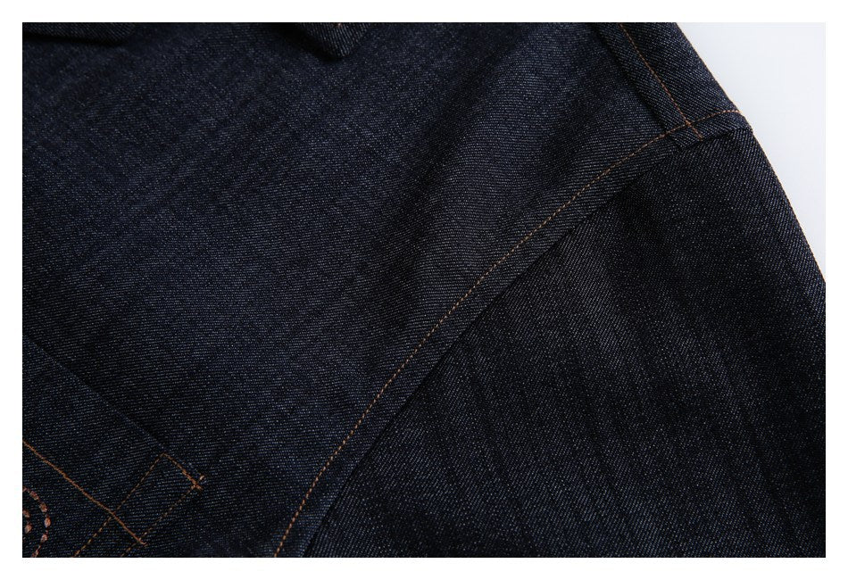 Close-up of dark indigo denim with curved seams and contrasting brown stitching.