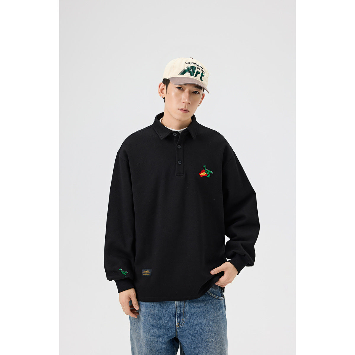 Model wearing a black collared pullover with a colorful embroidered chest motif and sleeve detail; medium front view.