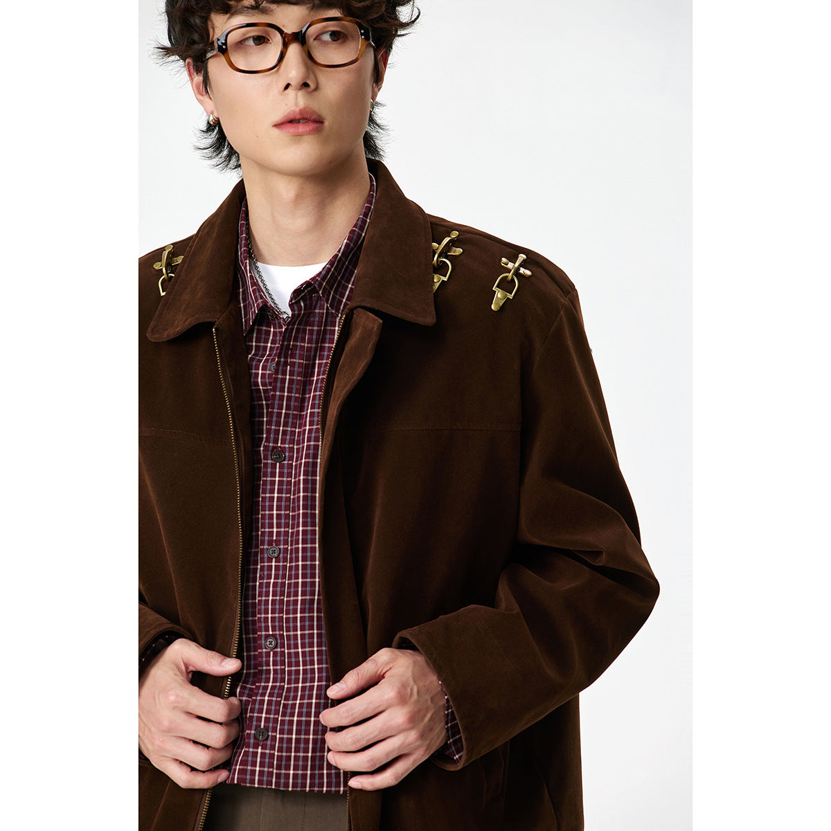 Close-up of a model wearing a dark brown jacket with gold shoulder hardware over a burgundy plaid shirt.