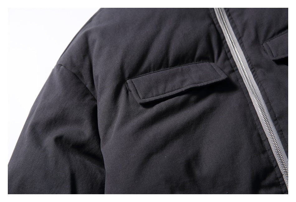 Close-up of a black jacket's flap chest pocket beside its silver front zipper.