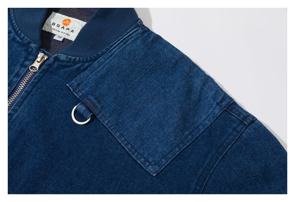 Close-up of a dark blue denim jacket shoulder with a flap pocket, metal ring, zipper, and inner neck label.