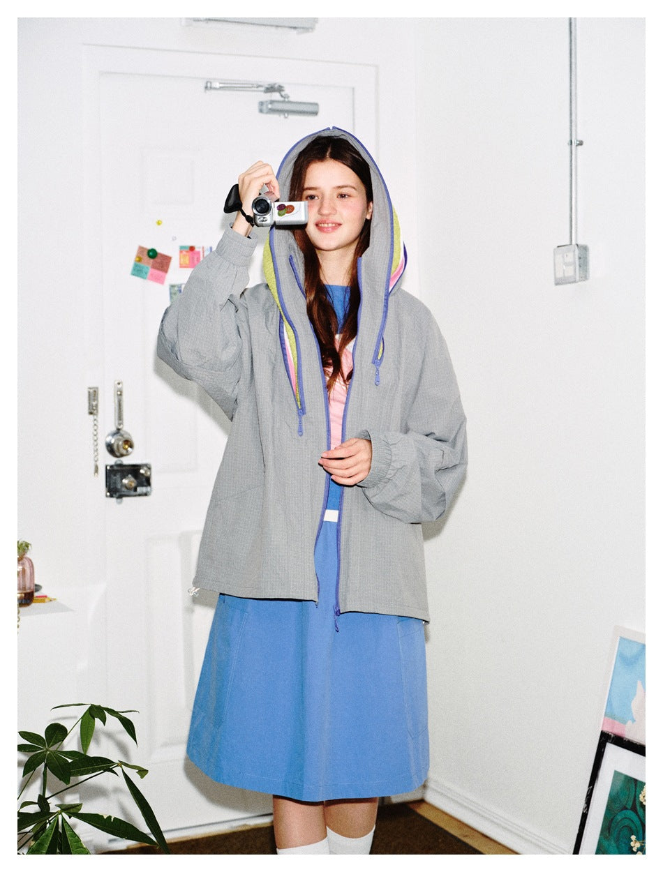 Model wears a gray hooded jacket with blue trim and yellow-pink lining over a blue dress.