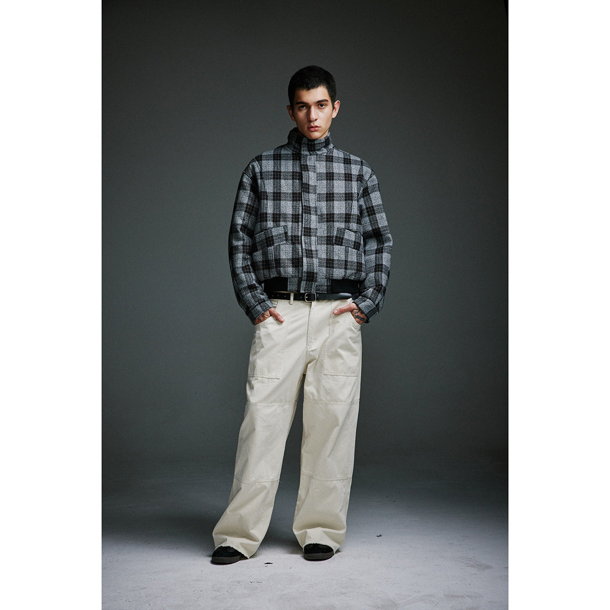 Model wearing a gray-and-black plaid high-neck zip jacket with cream wide-leg trousers.