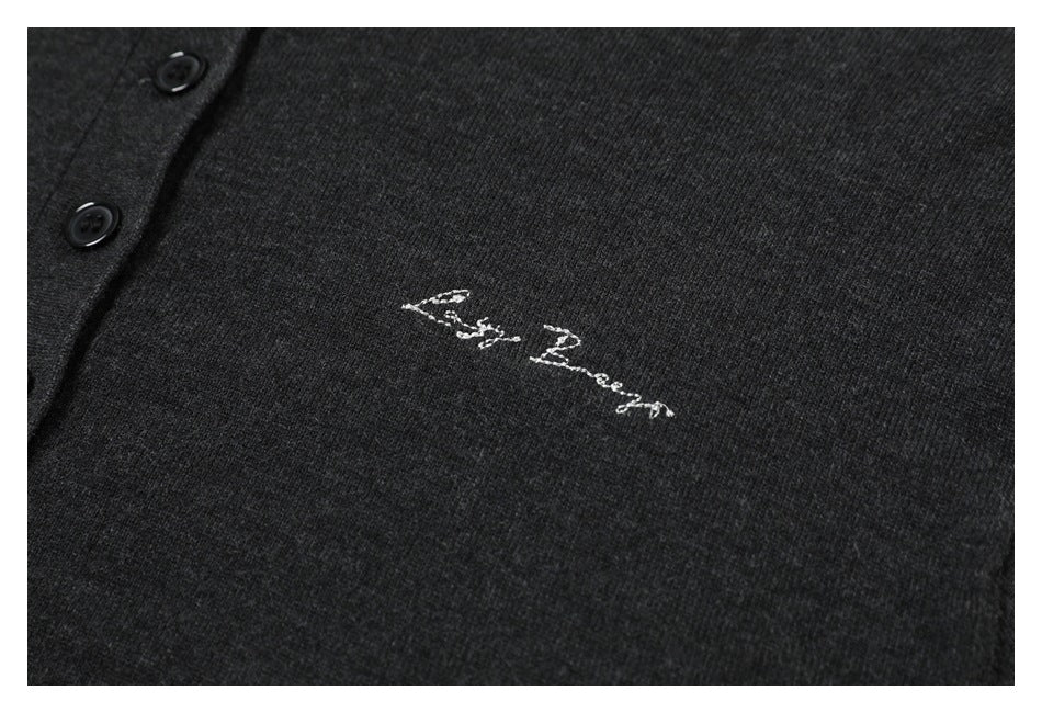 Close-up of white cursive embroidery on charcoal knit fabric near the button placket.