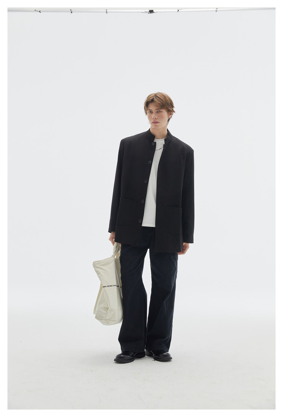 Model wearing a black stand-collar button jacket with patch pockets, white shirt and wide black cargo pants.
