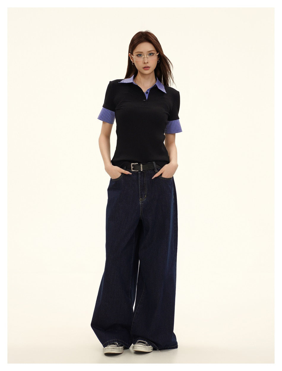 Model wearing black ribbed polo top with blue plaid collar and cuffs, wide-leg dark jeans and black belt