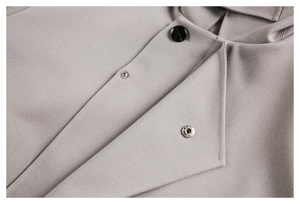 Light gray garment placket detail showing a black button and two metal snaps.