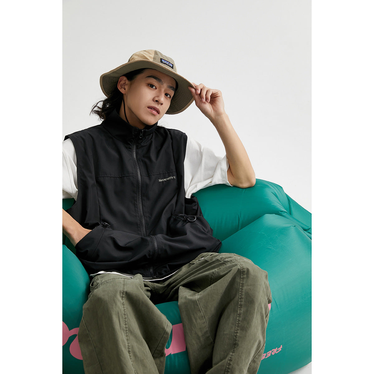 Model seated in a black sleeveless zip vest with a high collar and drawcord pockets.