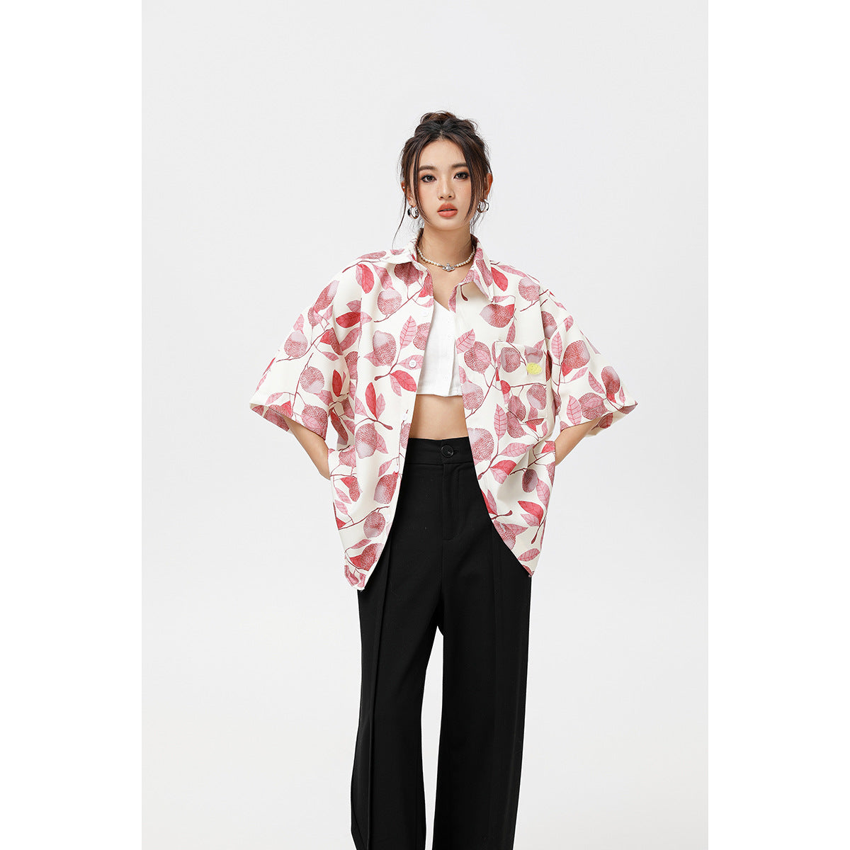 Model wearing an open white short-sleeve shirt with a pink leaf print over a white top and black trousers.