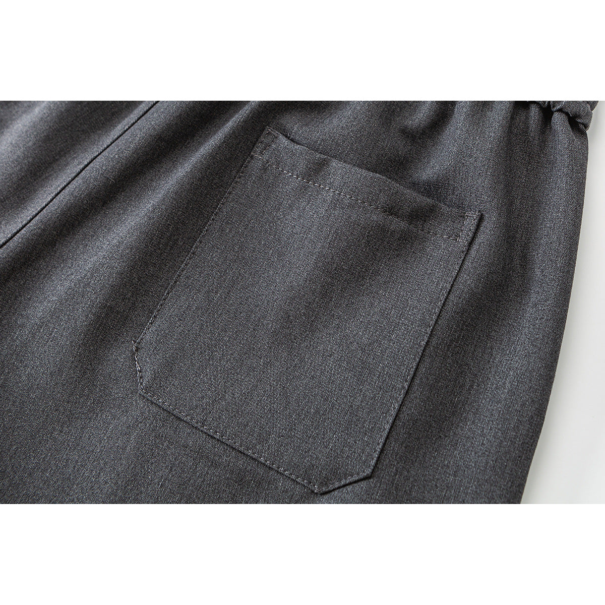 Close-up of a stitched patch pocket on dark gray trousers.