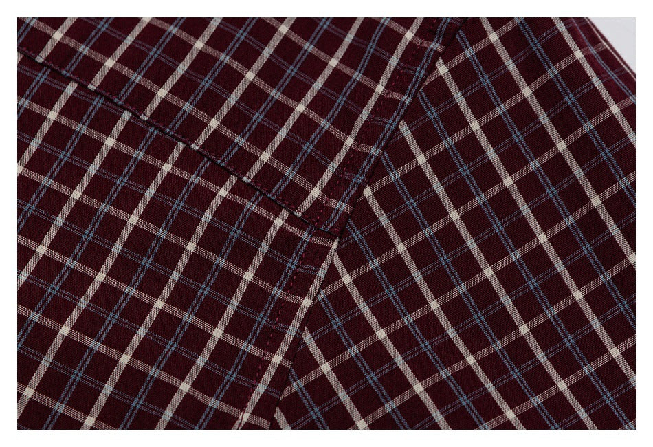 Close-up of intersecting shirt seams on burgundy fabric with a cream and blue plaid pattern.