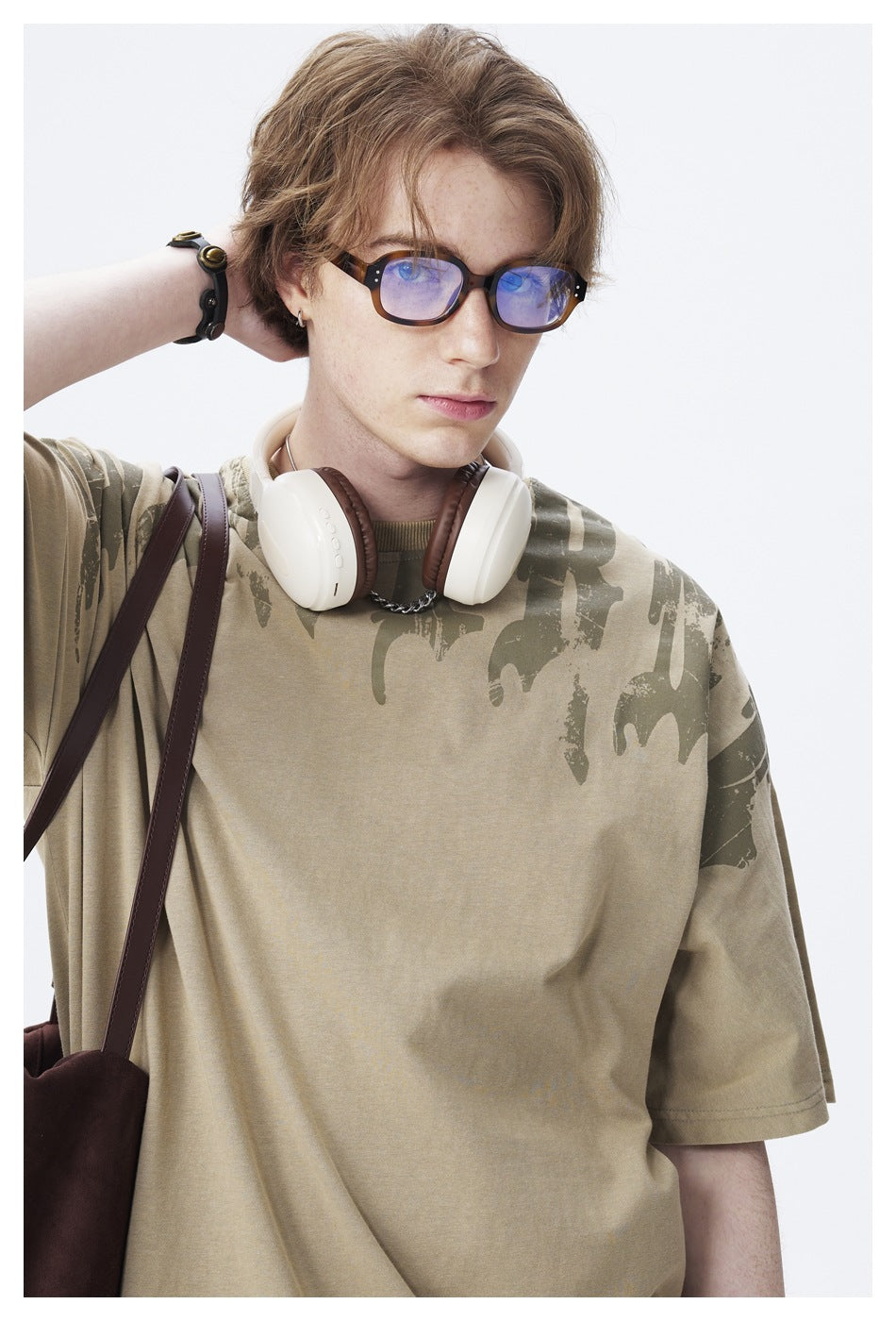 Close-up of a model wearing an olive oversized T-shirt with a dark abstract print across the shoulders.