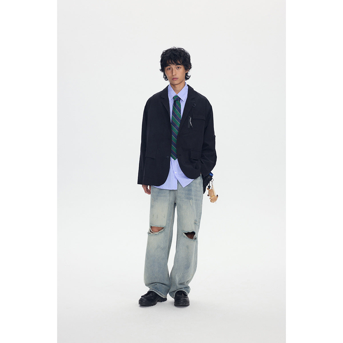 Full-length front view of a model in a black blazer, striped shirt and tie, and ripped light-wash jeans.