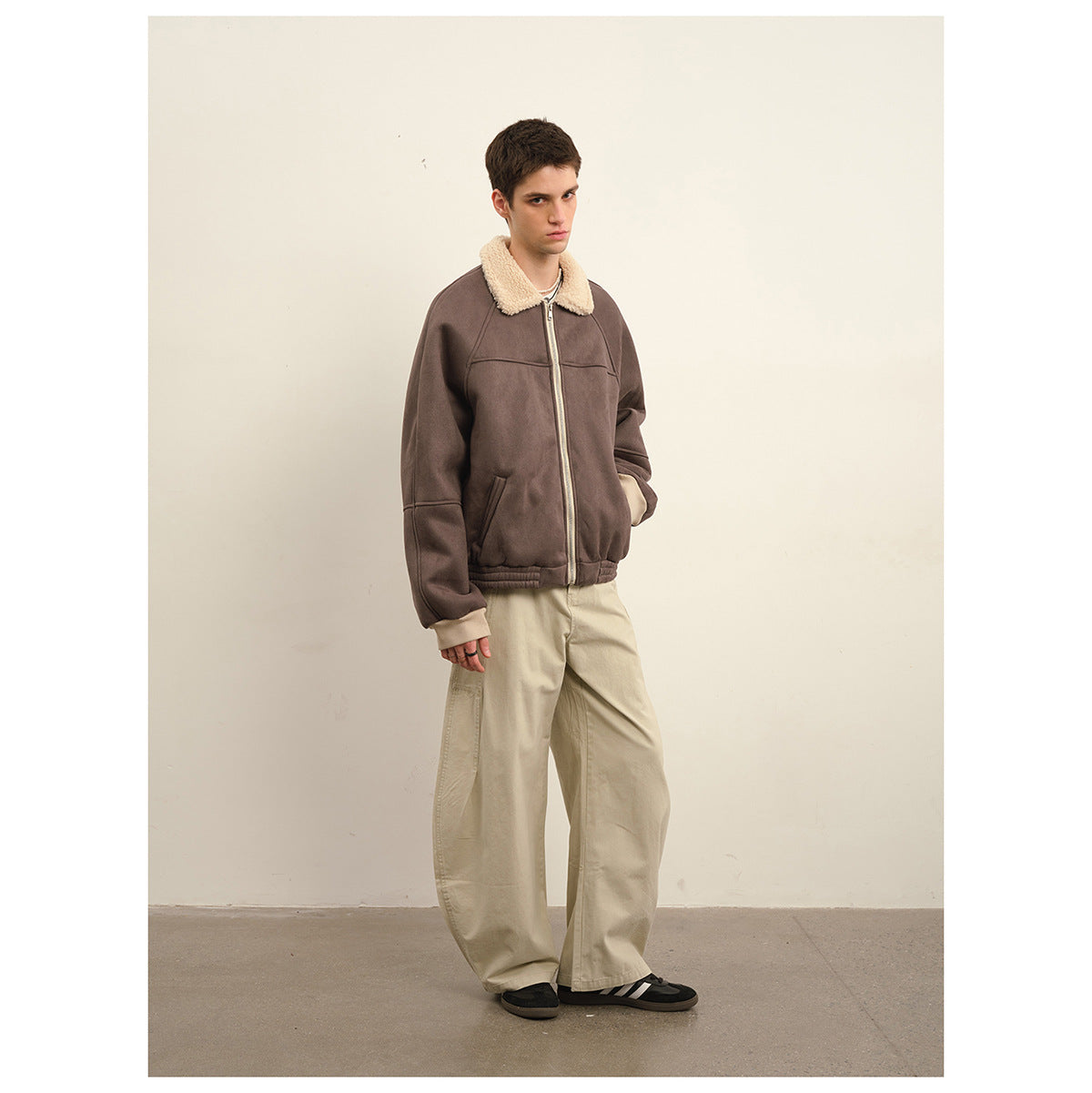 Model wearing a brown zip jacket with a cream shearling-style collar and loose beige trousers, full body.