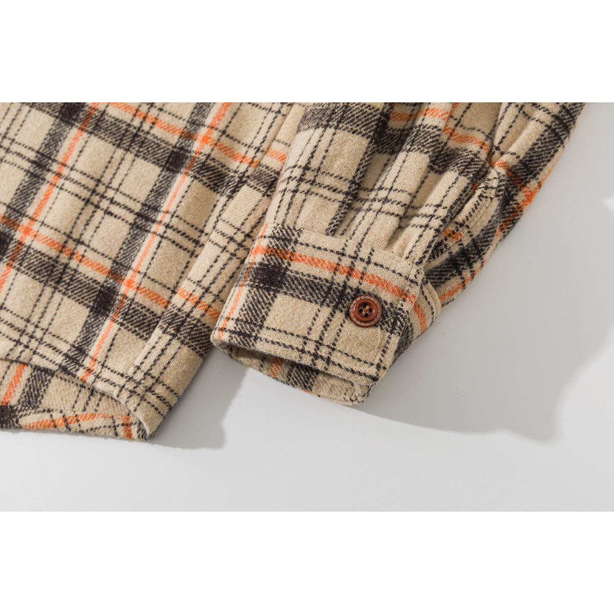 Close-up of a plaid shirt sleeve and buttoned cuff in beige, black, and orange.