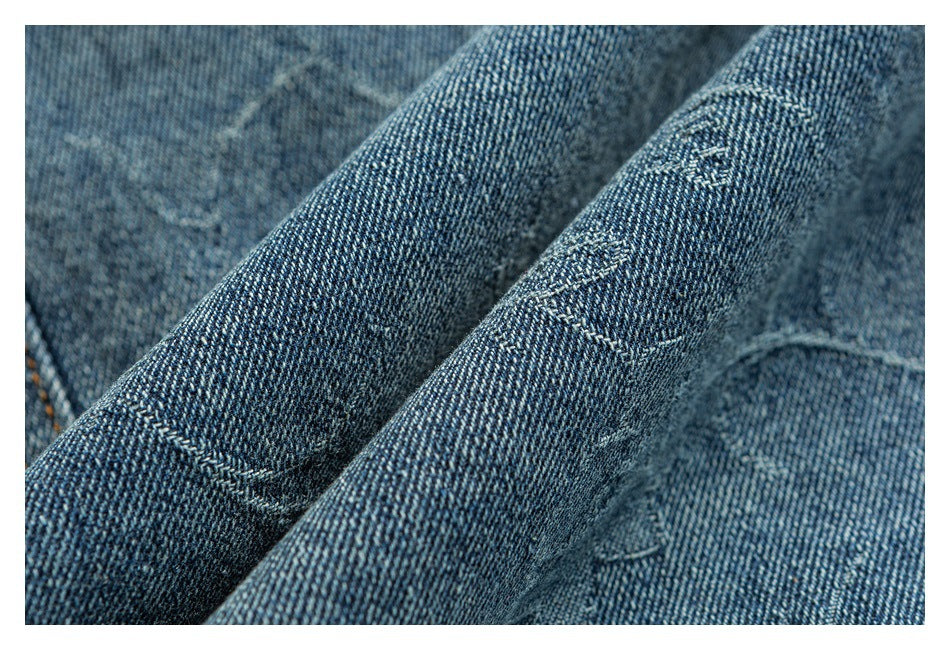 Close-up of blue denim fabric with subtle tonal stitched motifs.
