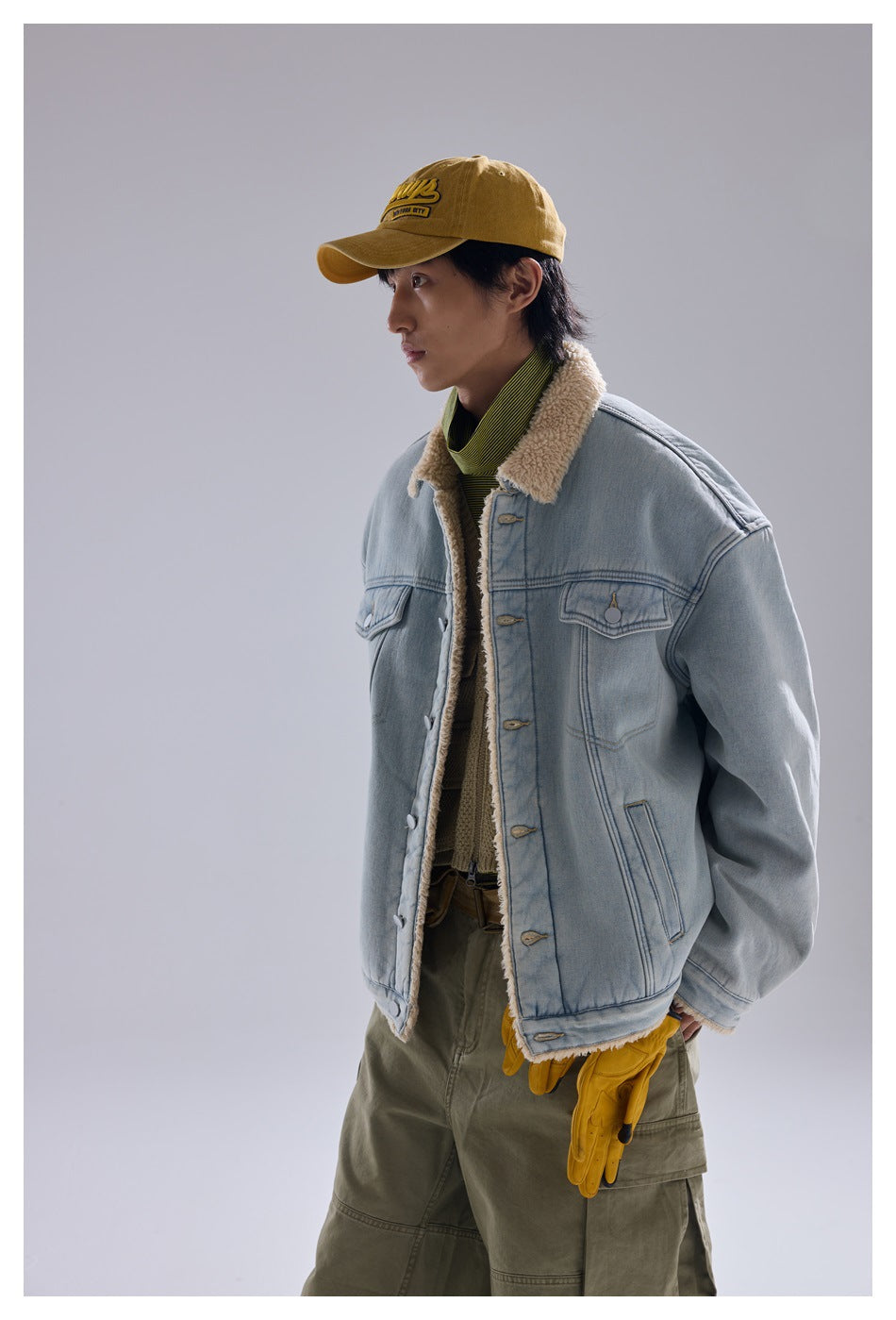 Side view of model in light blue denim jacket with cream fleece collar and lining, wearing cap and olive pants