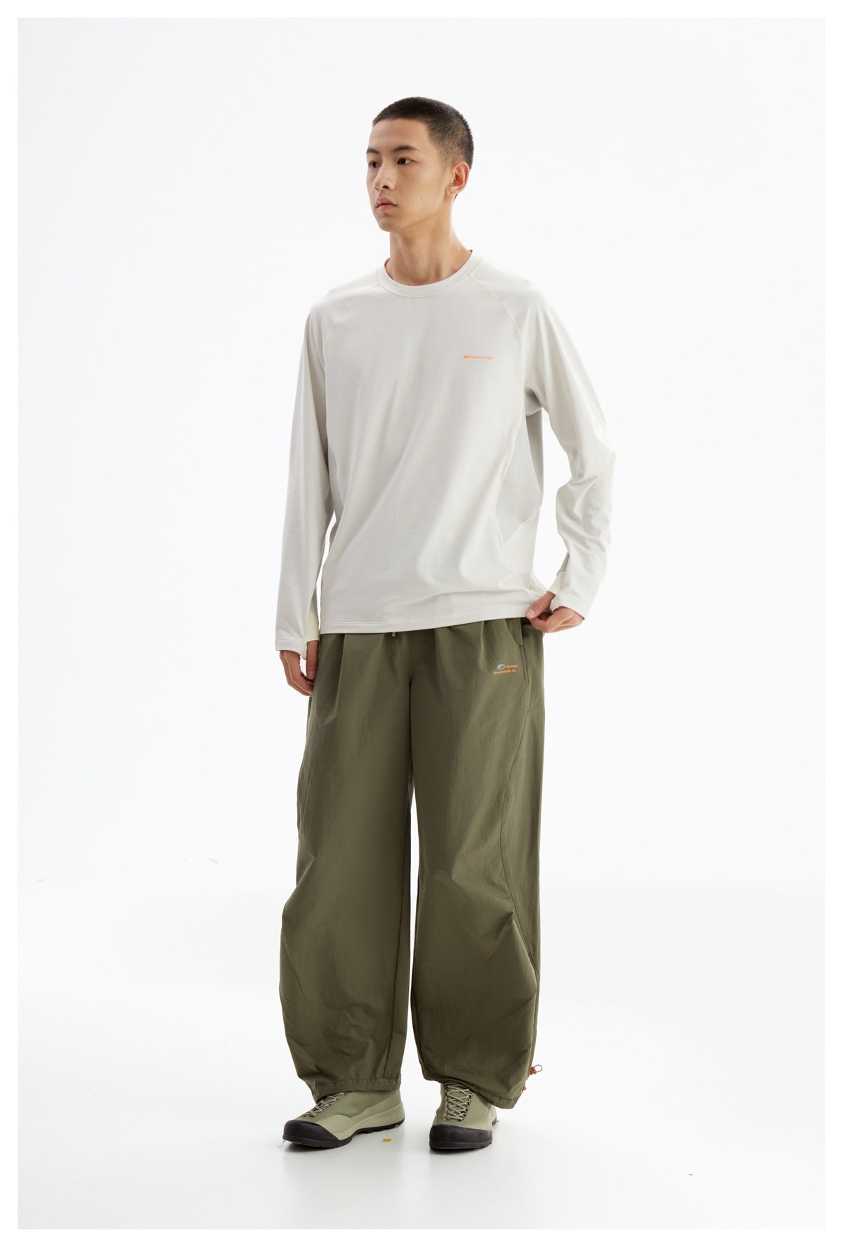 Model wearing a white long-sleeve crewneck shirt with olive wide-leg pants and hiking shoes.