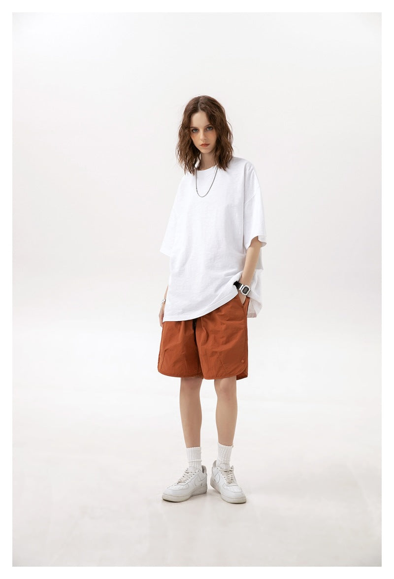 Model wearing rust-orange knee-length shorts with side pockets, a white oversized T-shirt, and sneakers.