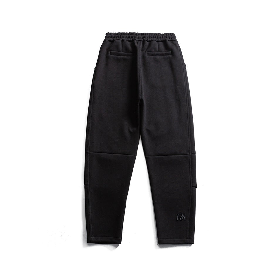 Back view of black tapered pants with an elastic waistband, two welt pockets, and panel seams.