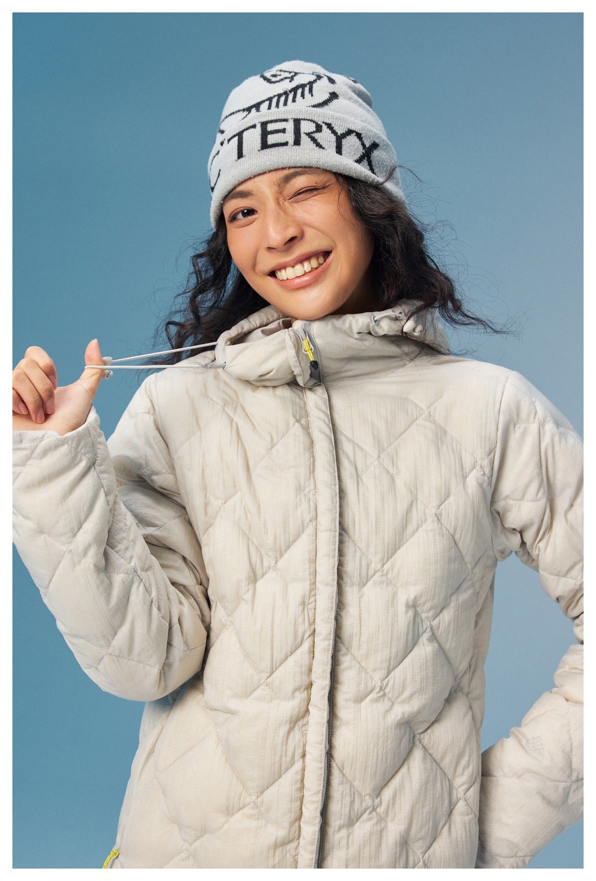 Close view of a cream diamond-quilted coat, its hood drawcord and high collar, worn by a model.