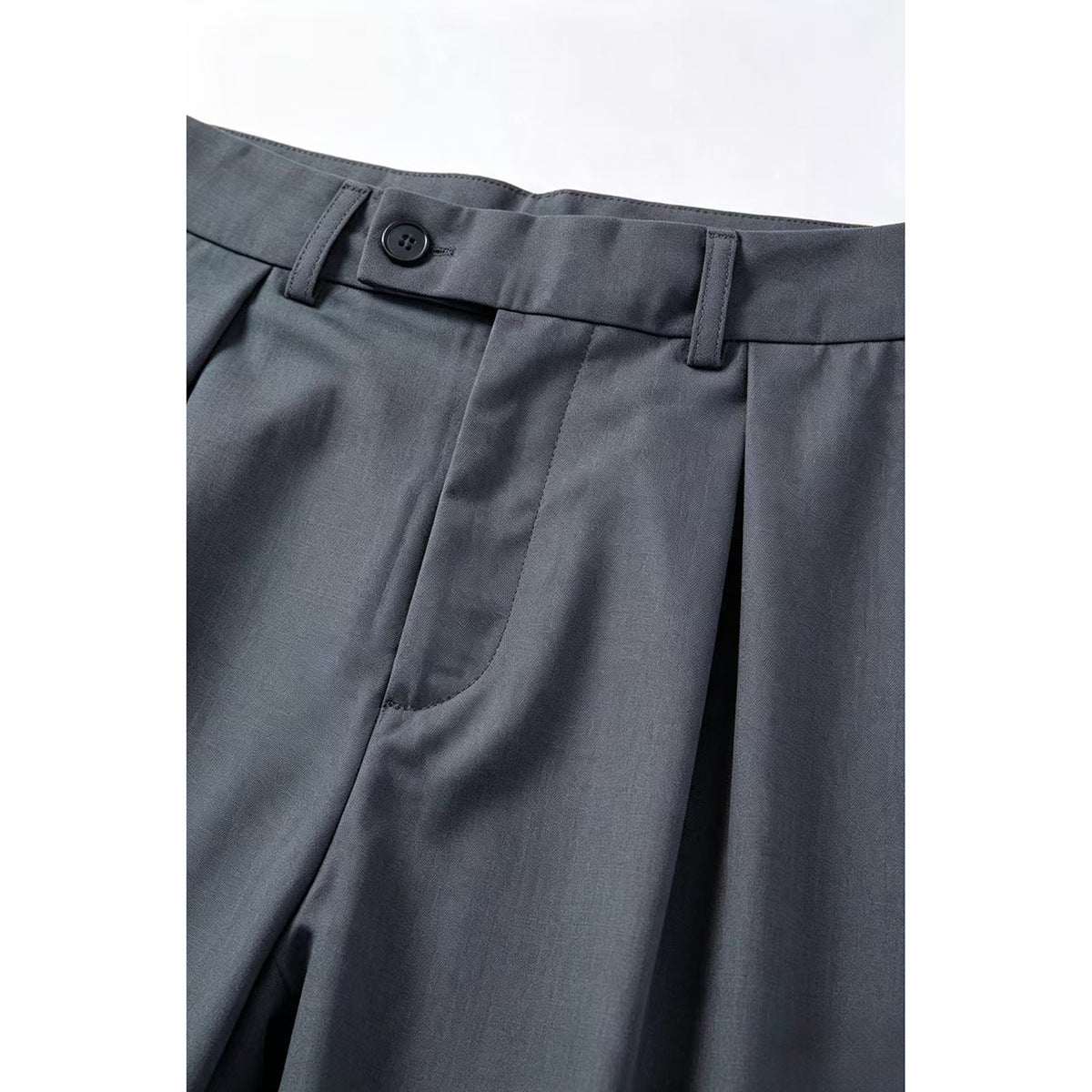 Close-up of charcoal-gray trousers showing a buttoned waistband, belt loops, pleats, and a front pocket opening.
