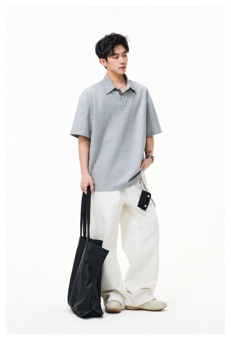 Model wearing an oversized light gray short-sleeve polo shirt with a textured collar and loose white trousers.