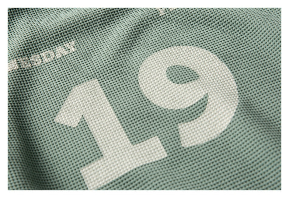 Close-up of a large white number 19 printed on sage-green textured fabric.