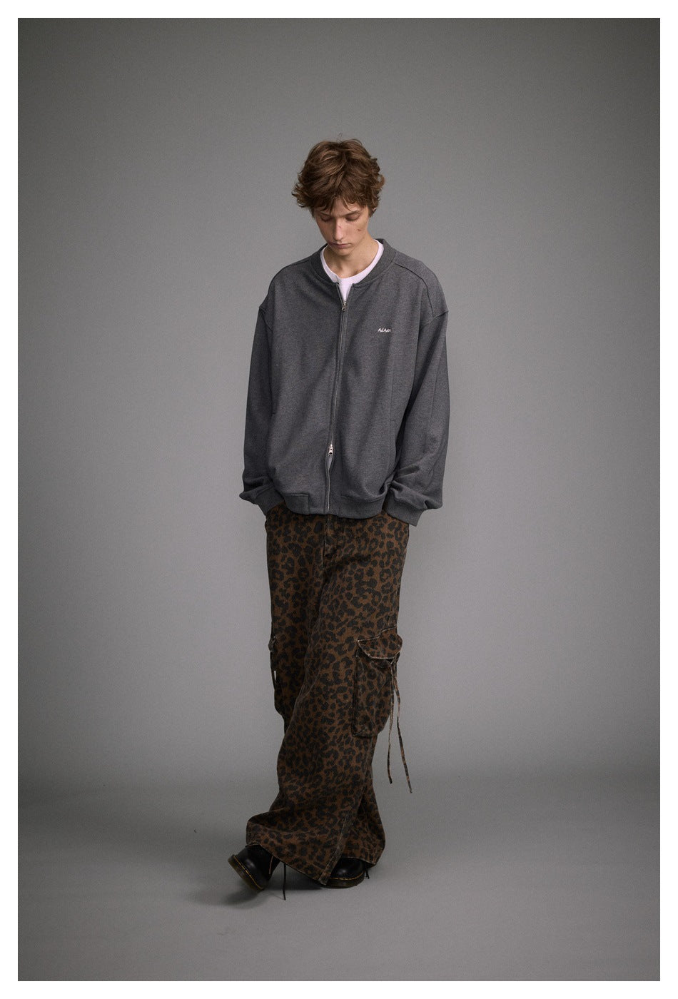 Front view of a model wearing an oversized charcoal gray zip-up jacket with a small chest logo and leopard-print cargo pants.