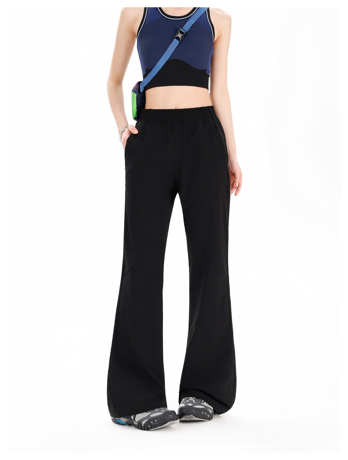 Woman wearing black flared pants with elastic waist and zip pockets, styled with a blue crop top and sneakers