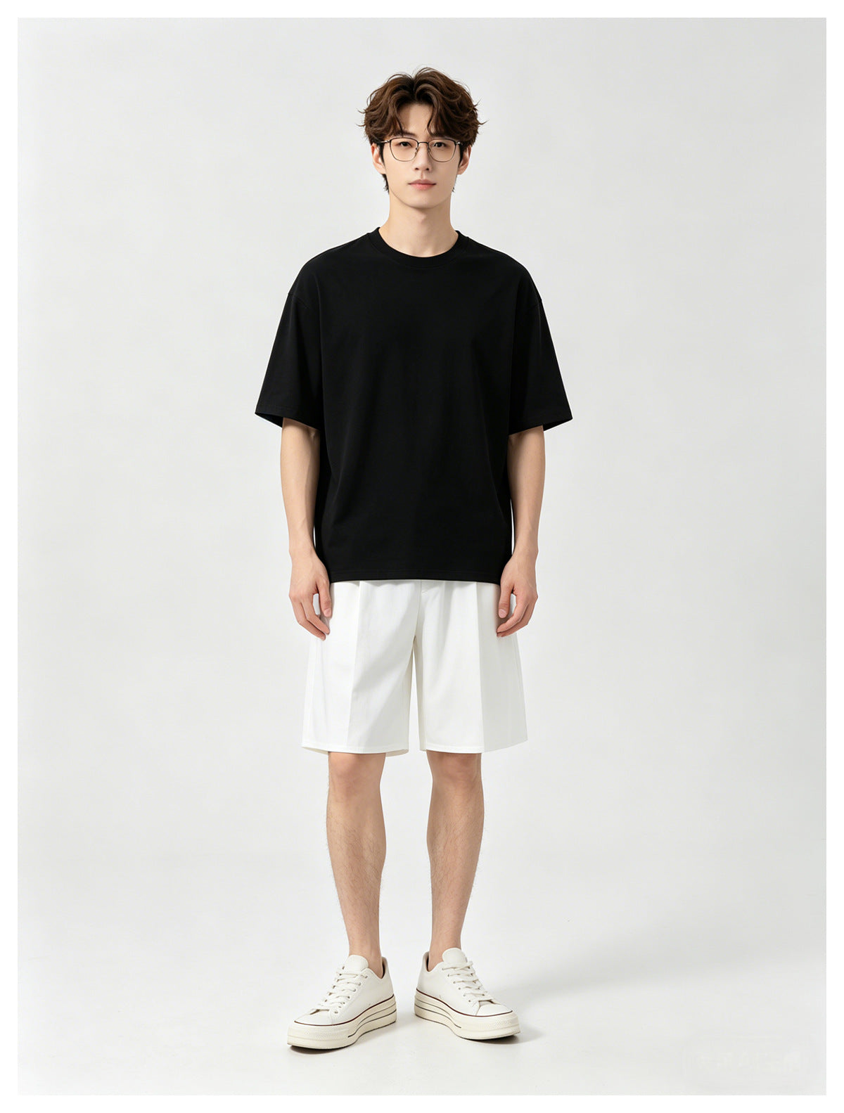 Front view of a model in a black crew-neck T-shirt, white shorts and white sneakers.