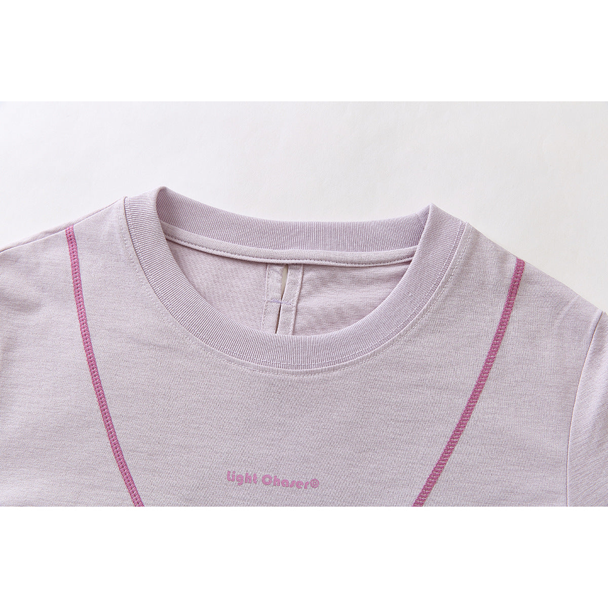 Close-up of a pale lavender crew neck top with pink contrast seams and small pink chest lettering.