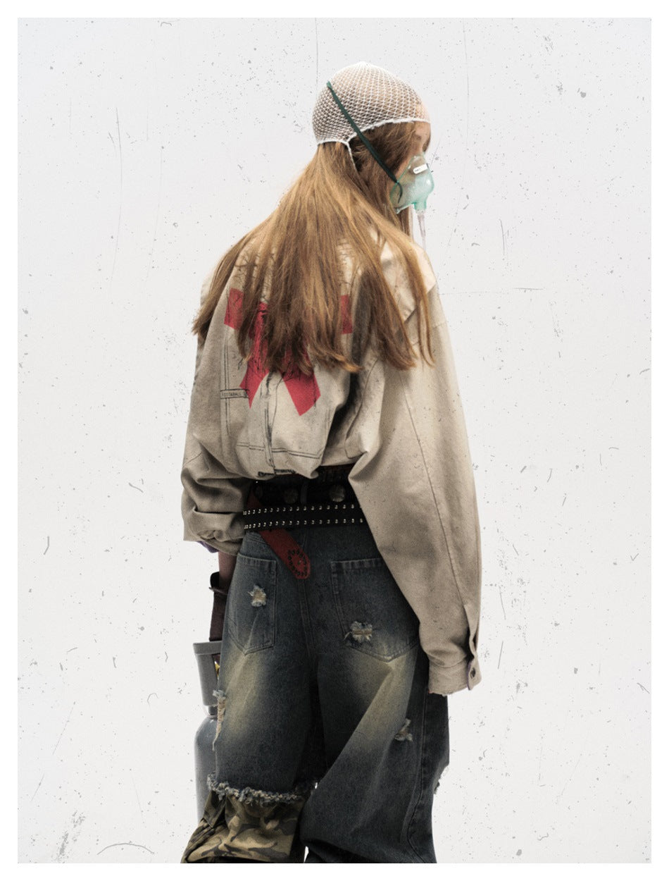 Rear view of a model wearing the beige jacket with a red back graphic and loose dark denim bottoms.