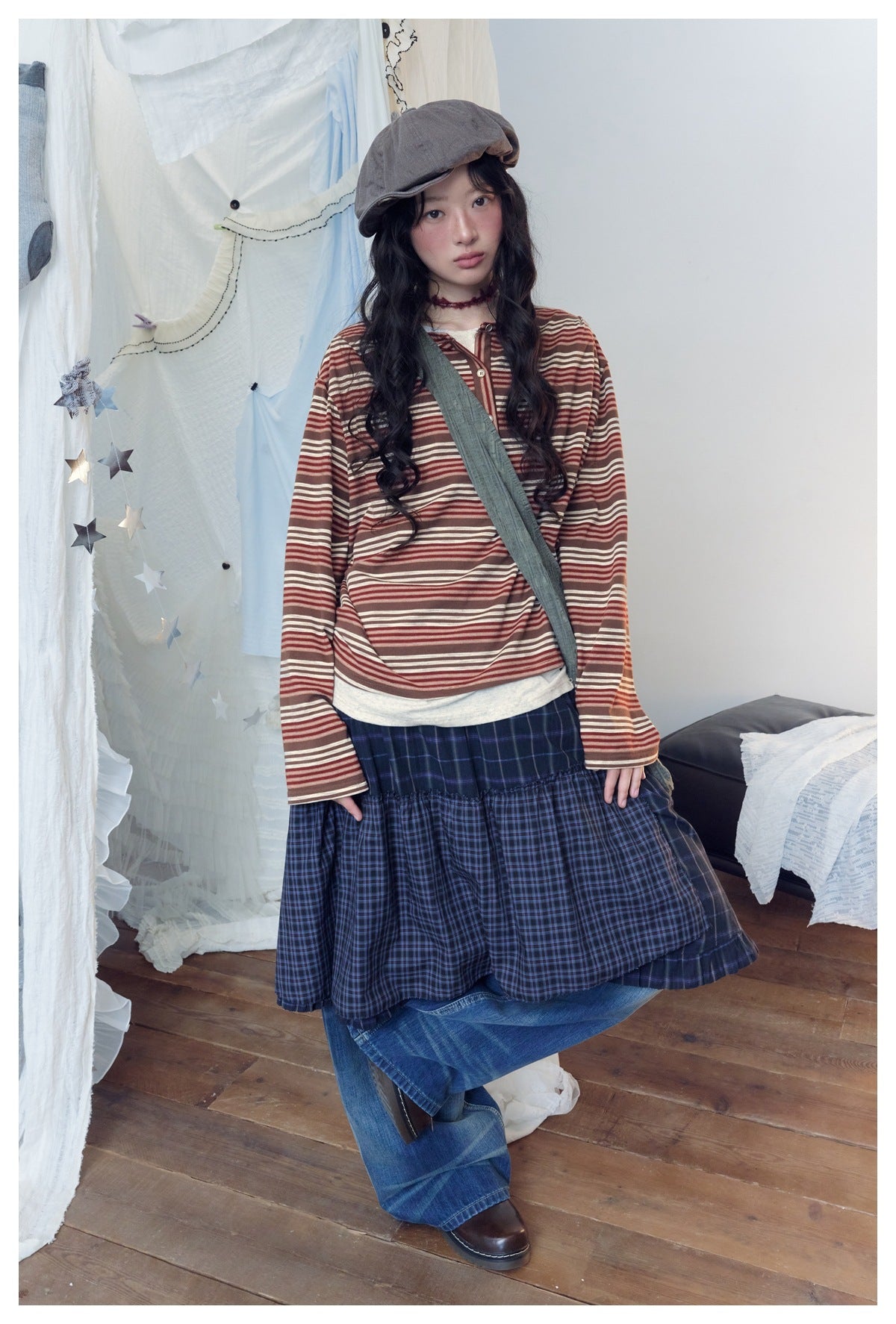 Full-length model wearing a rust and cream striped henley, navy plaid tiered skirt and wide-leg blue jeans.