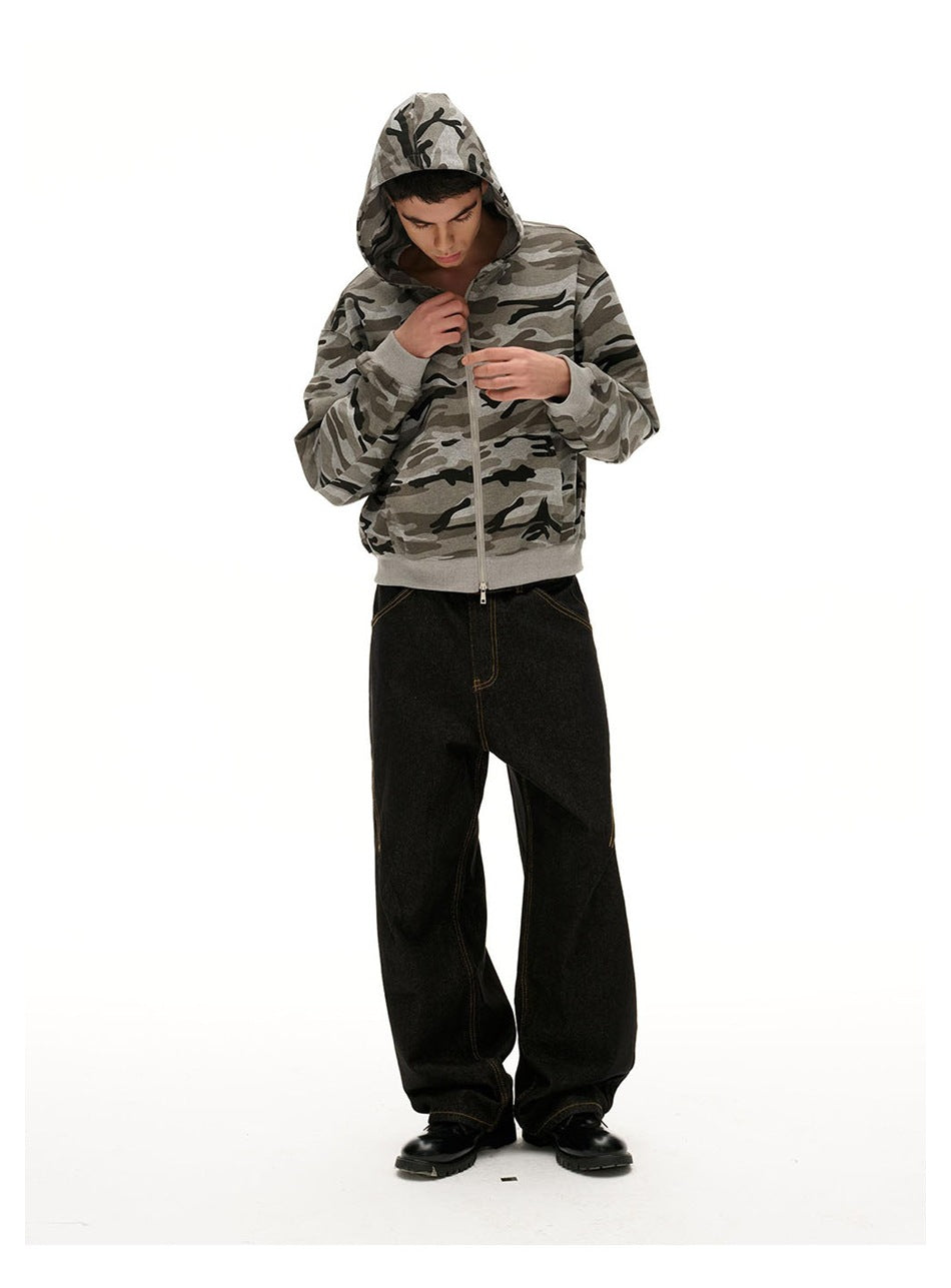 Model in a camouflage hooded zip jacket and black wide-leg jeans with black boots, looking down