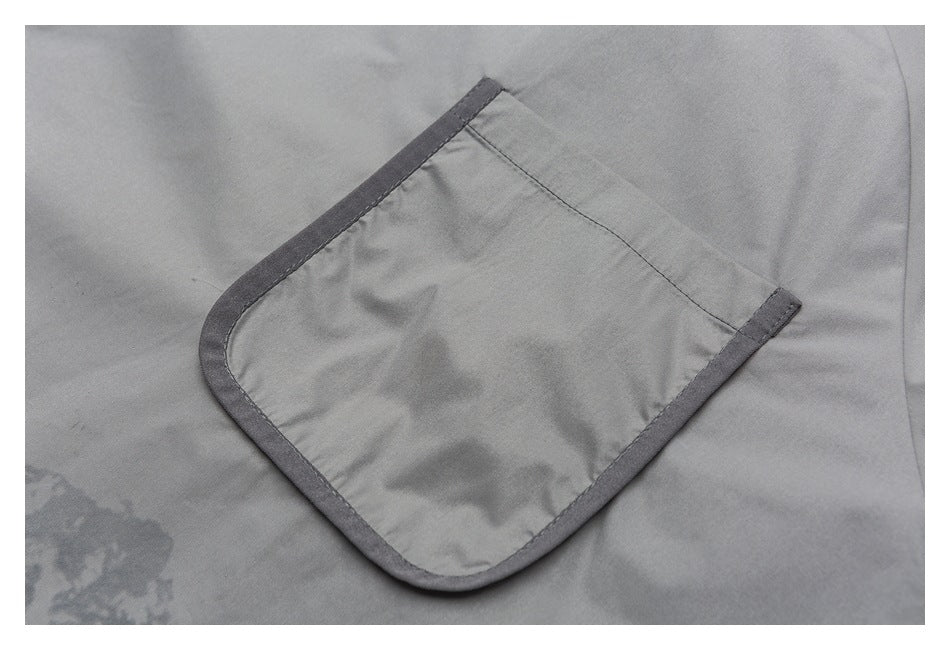 Close-up of a gray garment's large patch pocket with dark trim and a rounded lower edge.