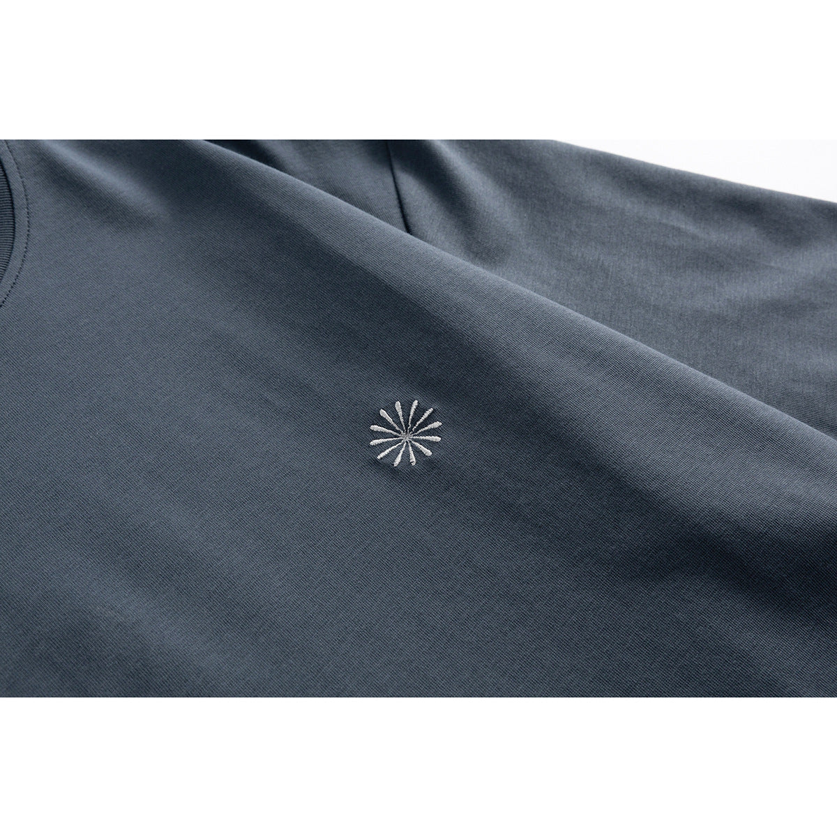 Close-up of a small white starburst embroidery on a dark slate blue T-shirt.